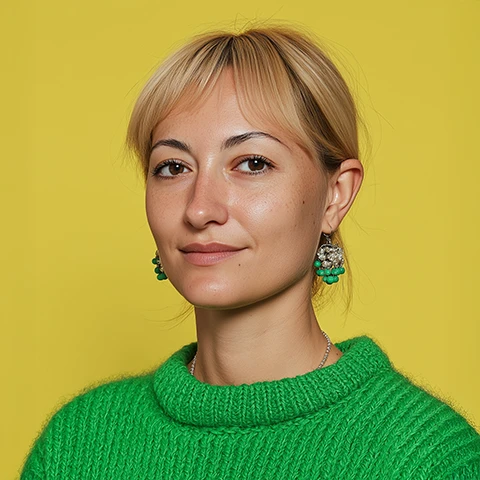 Smiling woman with short blonde hair wearing a bright green sweater and green beaded earrings against a yellow background.